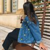 Femme portant une veste en jean avec de la broderie motifs citrons, sur un banc, en extérieur